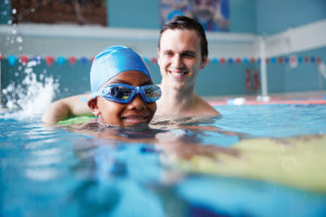 Male Swimming Coach Giving Boy Holding Float One To One Lesson I